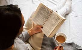 Frau liest ein Buch und trinkt einen Kaffee auf dem Bett